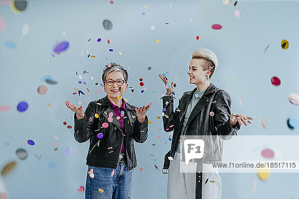 Happy mature woman throwing confetti with daughter in front of wall