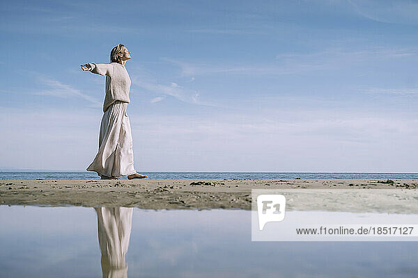 Woman walking with arms outstretched at beach