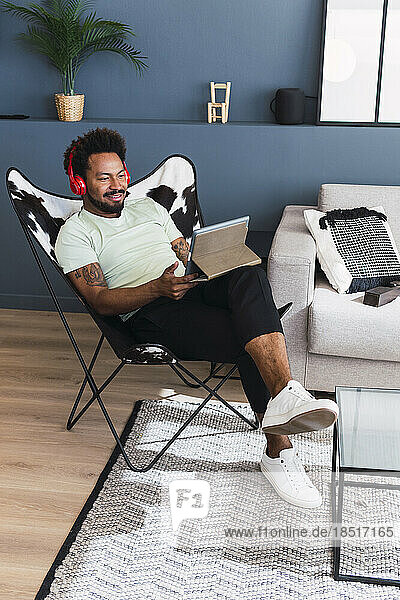 Mann sitzt zu Hause auf einem Stuhl und schaut sich einen Tablet-PC an