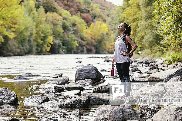 Frau mit der Hand auf der Hüfte genießt die Natur in der Nähe des Flusses