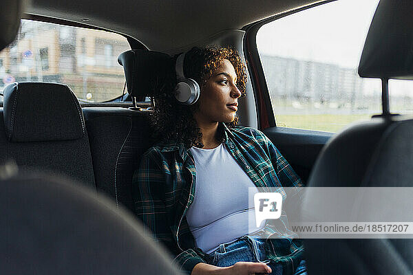Thoughtful woman wearing bluetooth headphones in car