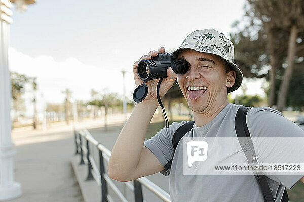 Happy man sticking out tongue and looking through binoculars