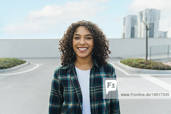 Happy young woman with curly hair standing on footpath
