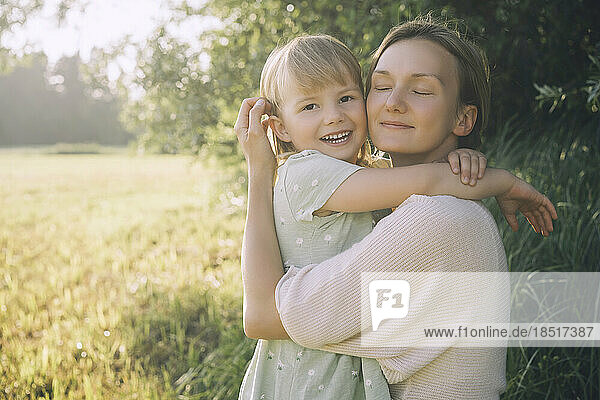 Lächelnde Mutter umarmt ihre Tochter an einem sonnigen Tag in der Natur