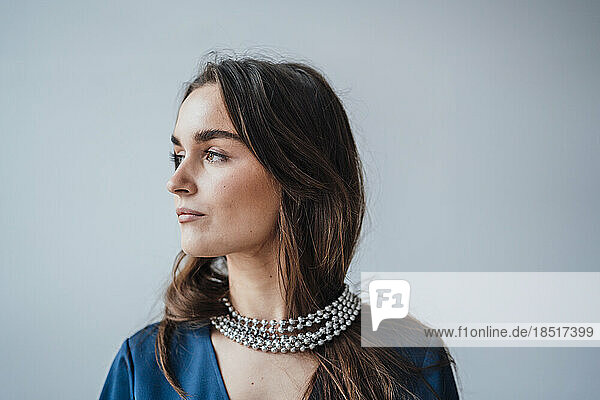 Thoughtful businesswoman wearing silver jewelry in front of wall
