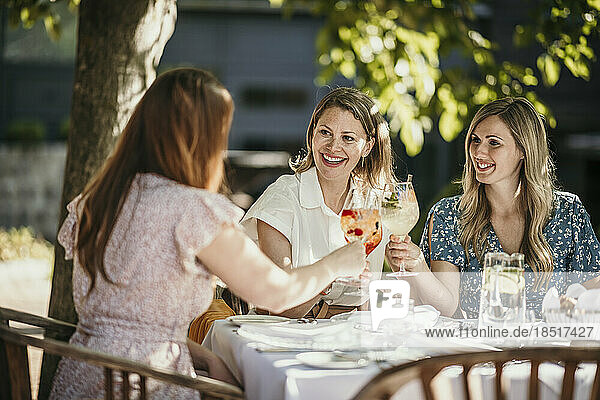 Happy female friends toasting drinks sitting at table in restaurant