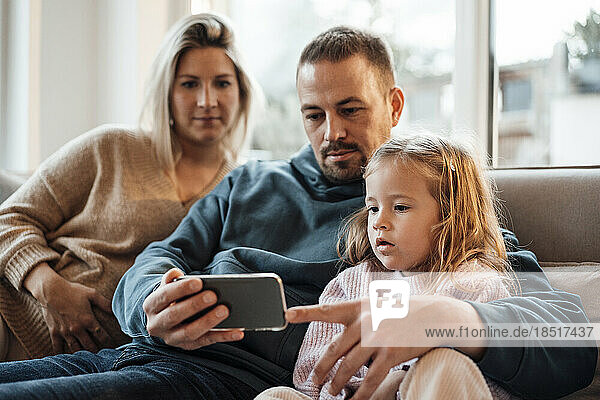 Father sharing mobile phone with daughter at home