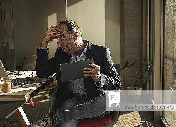 Schockierter Geschäftsmann mit Kopf in der Hand blickt im Büro auf Laptop