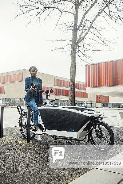 Businesswoman using smart phone sitting on cargo bike