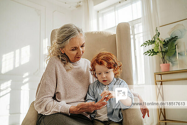 Boy touching hand of grandmother sitting on armchair at home
