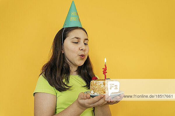 Girl blowing candle on birthday cake against yellow background