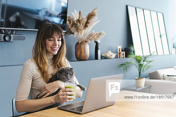 Happy woman watching laptop with cat at home