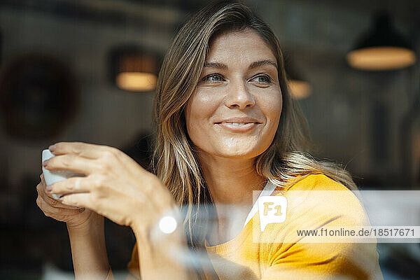 Smiling woman with coffee cup in cafe seen through glass