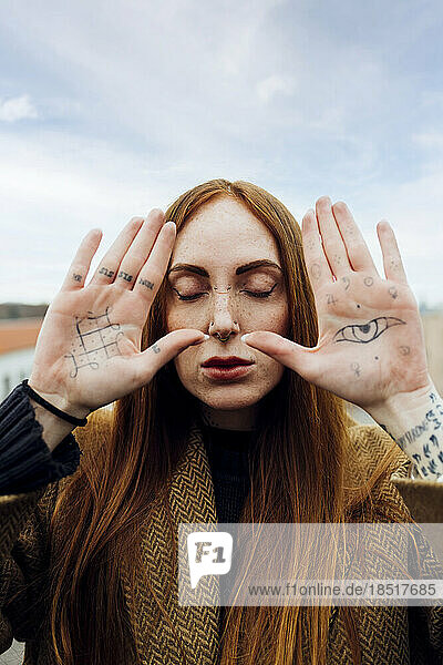 Woman with eyes closed showing tattoo on palm of hands
