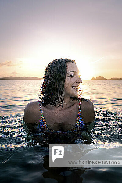 Lächelnde junge Frau  die sich bei Sonnenuntergang im Wasser amüsiert