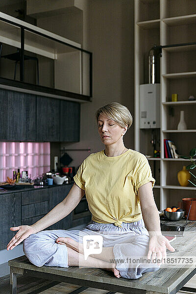 Frau praktiziert Yoga und meditiert im Schneidersitz zu Hause