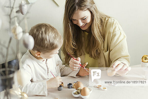 Happy mother and son decorating Easter eggs at home