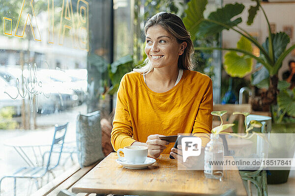Happy woman with credit card holding mobile phone sitting in cafe