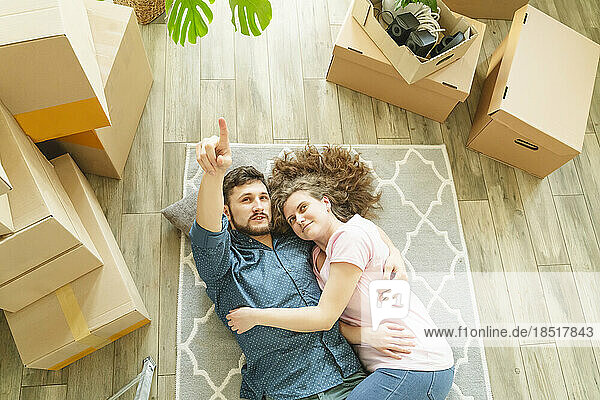 Young man gesturing girlfriend lying on carpet in new home