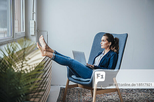 Thoughtful businesswoman sitting on armchair with laptop