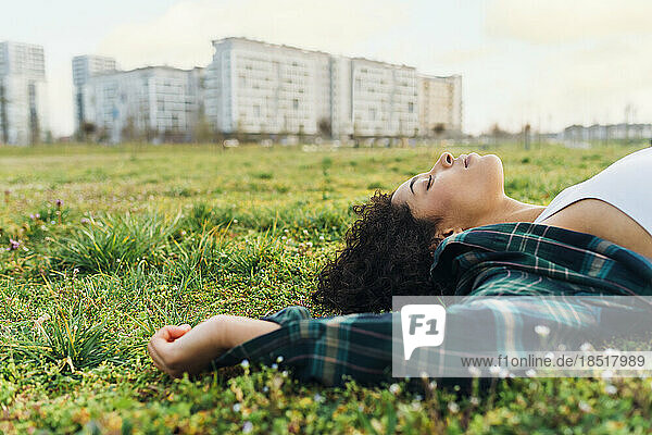 Young woman with eyes closed relaxing in grass at sunset