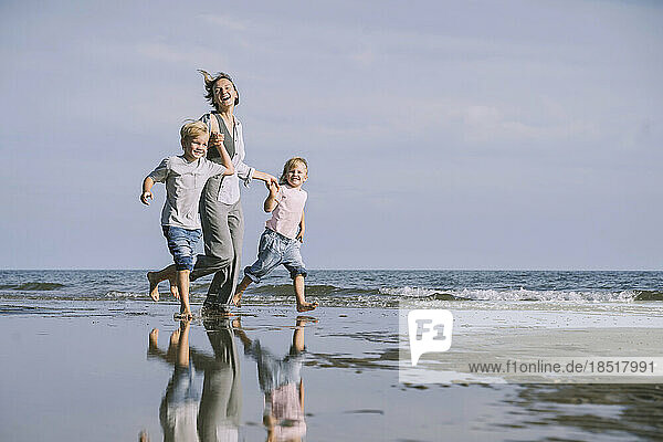 Happy mother running with daughter and son on shore at beach