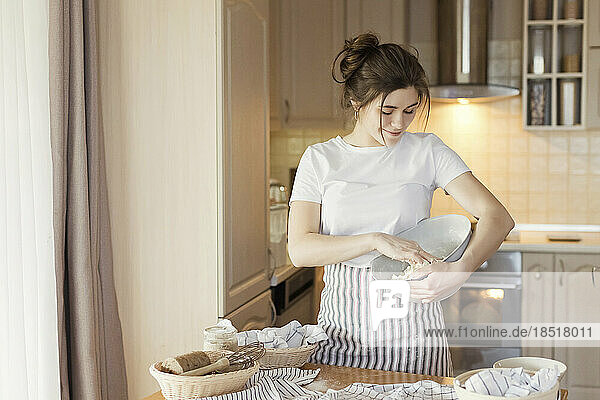 Smiling young woman kneading bread dough in bowl
