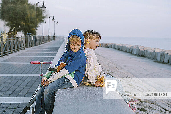 Smiling boy sitting with sister on promenade at sunset