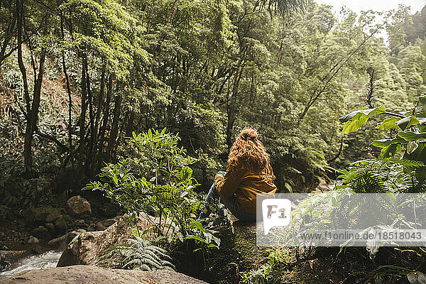Young redhead woman sitting on rock in forest