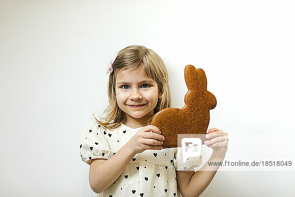 Smiling girl holding gingerbread Easter bunny against white background