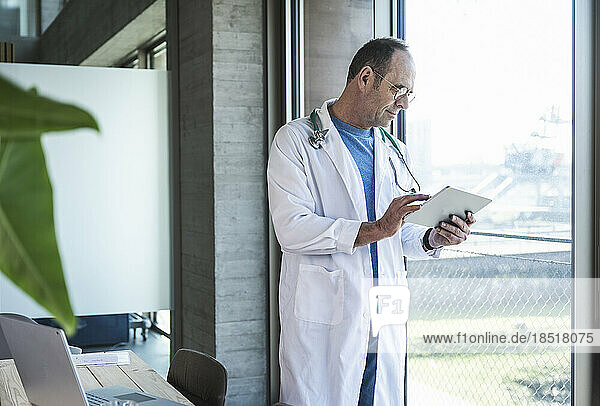 Doctor using tablet computer standing by window