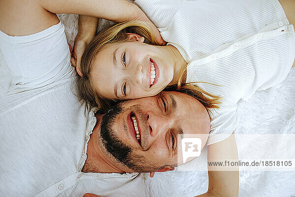 Happy father and daughter lying on bed at home