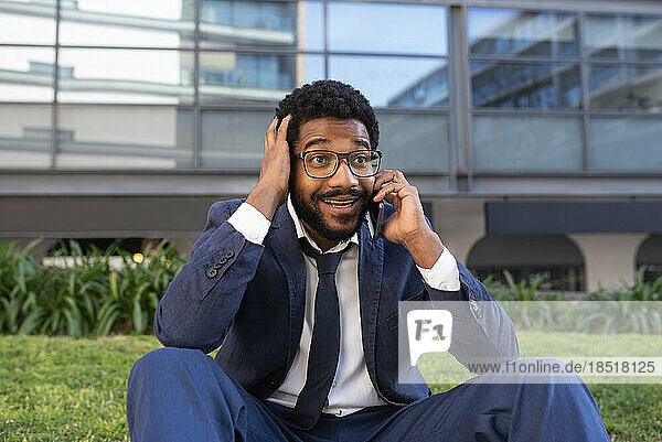 Überraschter Geschäftsmann mit Kopf in den Händen  der vor dem Bürogebäude mit dem Mobiltelefon spricht