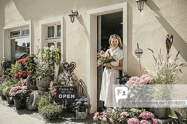 Mature woman with flowers standing near doorway of flower shop