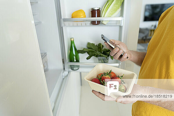 Älterer Mann hält frische Erdbeeren und Smartphone zu Hause