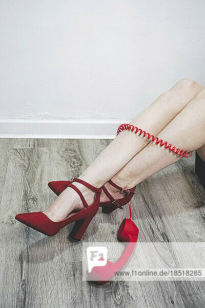 Legs of woman wearing red heels surrounded by telephone receivers cord