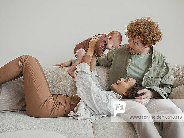 Frau spielt mit Baby und Mann sitzt zu Hause auf dem Sofa