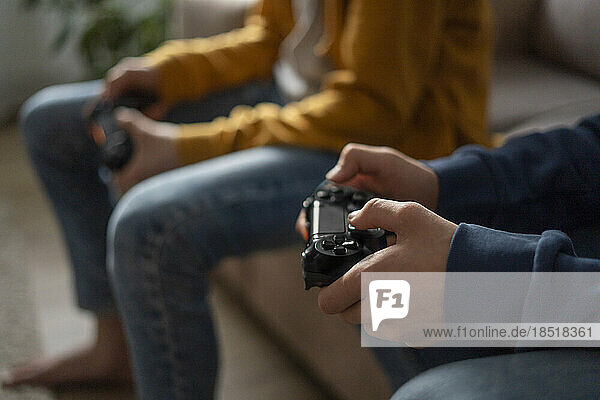Hands of boys holding gaming consoles at home