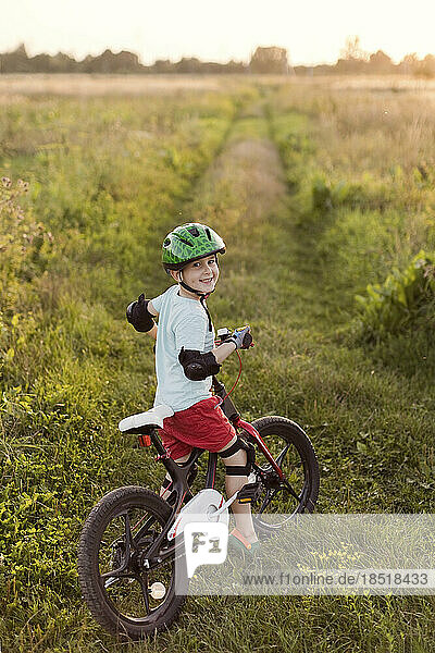 Smiling boy wearing helmet riding bicycle on field at sunset