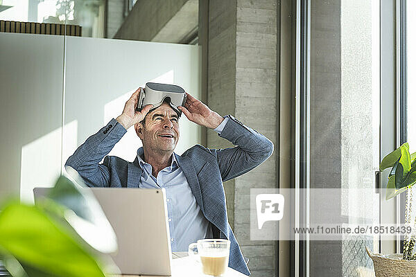 Mature businessman wearing virtual reality simulator sitting in office