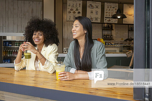 Smiling women sitting together with juice at table in cafe