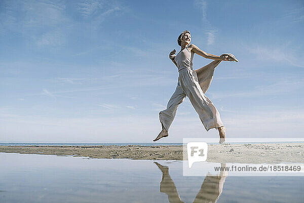 Reflection of happy woman jumping at beach