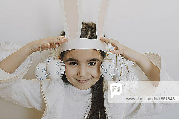 Smiling girl holding Easter eggs in front of wall
