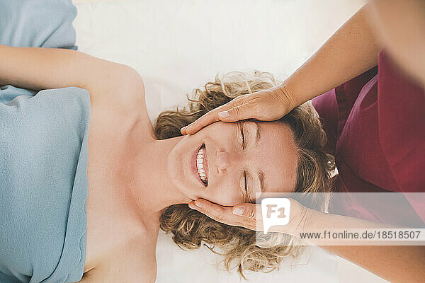 Therapist giving head massage to happy customer in salon