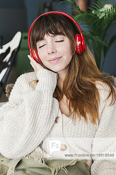 Frau mit geschlossenen Augen hört zu Hause Musik über kabellose Kopfhörer