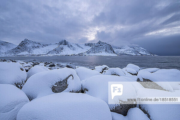 Norway  Troms og Finnmark  Snow covered boulders at Tungenest Rasteplass with fjord and snowcapped mountains in background
