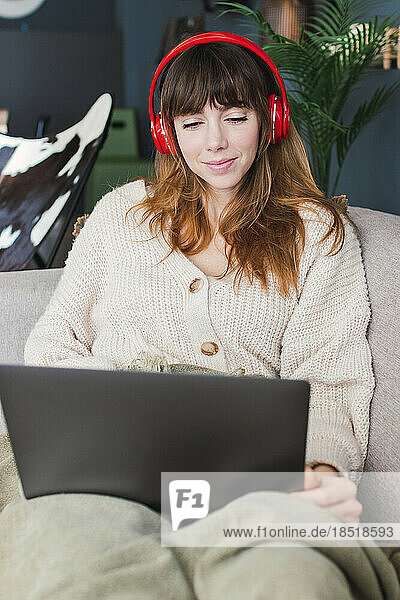 Woman wearing wireless headphones watching laptop at home