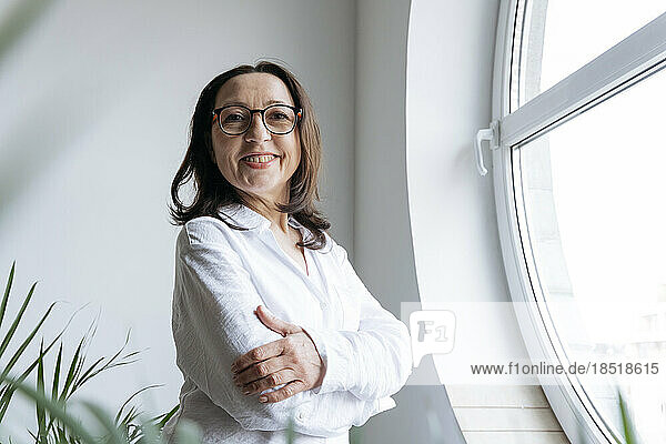 Confident mature businesswoman with arms-crossed at the window