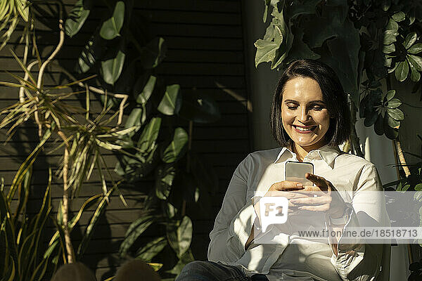 Glückliche Frau  die auf dem Balkon das Internet mit dem Mobiltelefon nutzt