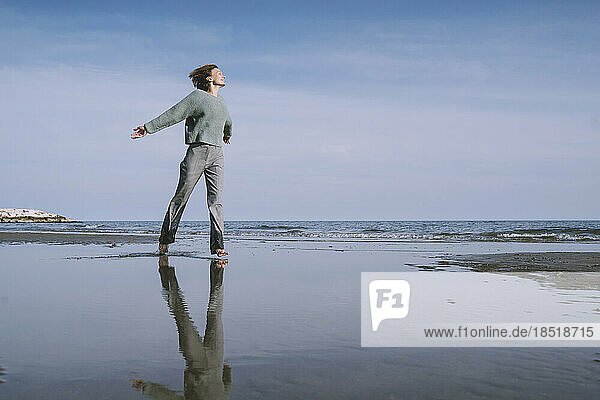 Reflection of woman with arms outstretched walking on shore at beach